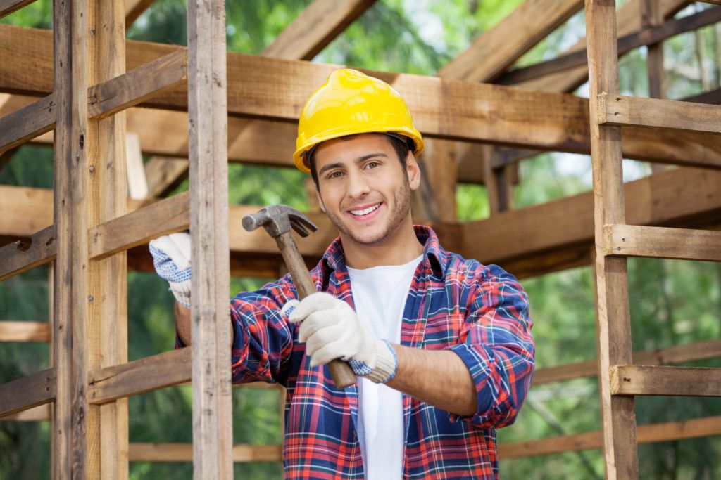 Carpentry Training for Youth - Portrait of a happy male construction worker holding a hammer in an incomplete wooden cabin. 