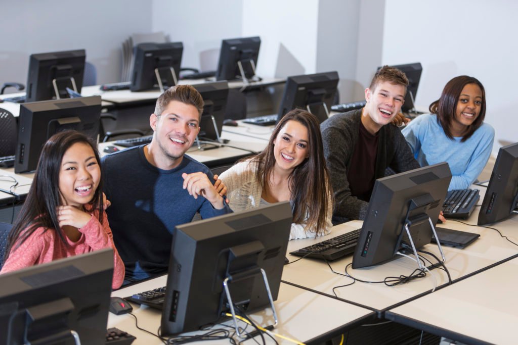 Completing the Circle - Five young people sitting in a row and smiling in a computer lab.